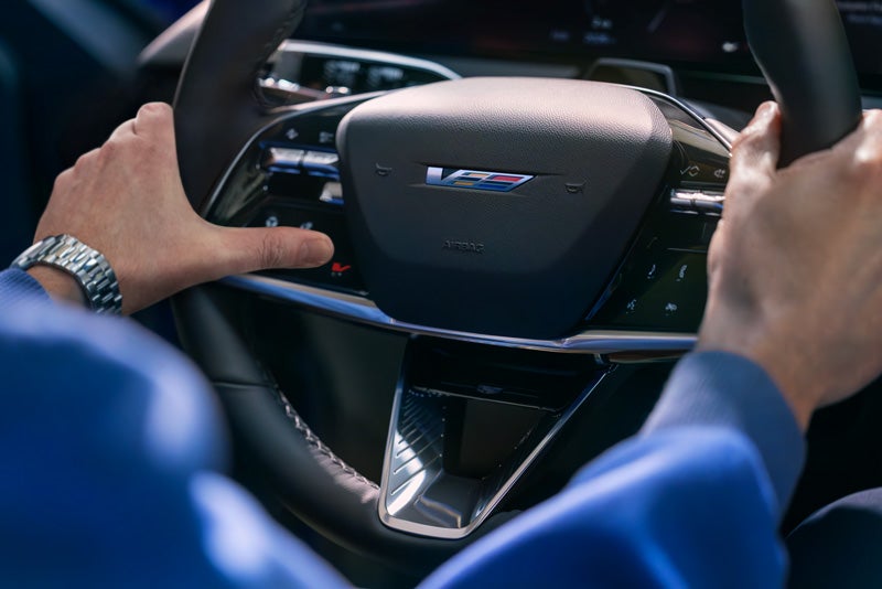 Close-up of a Man About to Press the V-Button on the 2026 OPTIQ-V Steering Wheel | Fitzgerald Cadillac Frederick in Frederick MD